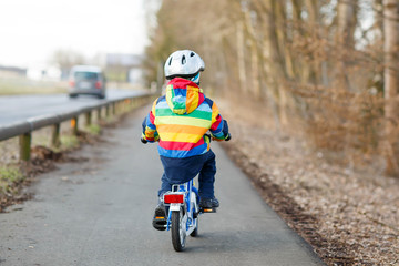 Fototapeta premium kid boy in safety helmet and colorful raincoat riding bike, outd