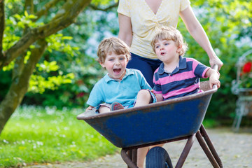 Two little boys having fun in a wheelbarrow pushing by mother