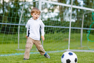 Two little sibling boys playing soccer and football on field