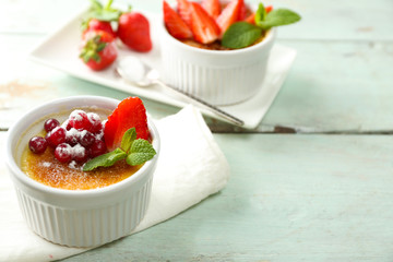 Creme brulee dessert with fresh strawberry berries on napkin, on color wooden background