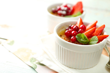 Creme brulee dessert with fresh strawberries and mint leaves, on color wooden background