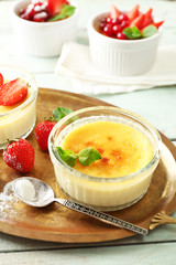 Creme brulee dessert with fresh strawberries and mint leaves, on color wooden background