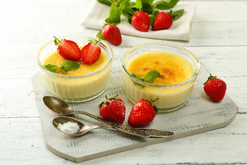 Creme brulee dessert with fresh strawberries and mint leaves, on color wooden background