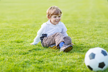 Two little sibling boys playing soccer and football on field