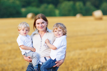 Young mother and two little twins boys having fun on yellow hay