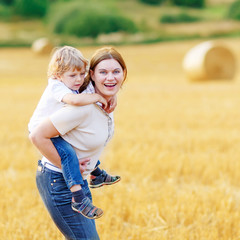 Young mother and her little son having fun on yellow hay field