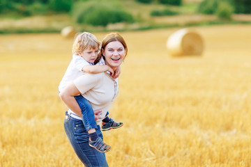 Naklejka na ściany i meble Young mother and her little son having fun on yellow hay field