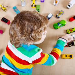 Little blond child playing with lots of toy cars indoor