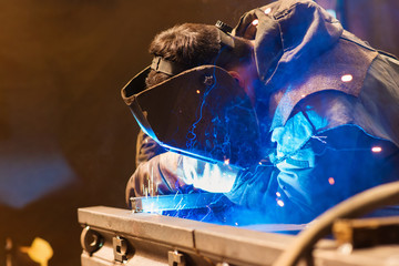 Young man welding inside in a factory - obrazy, fototapety, plakaty