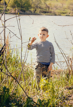 Boy Stopping to Smell Plant Along Shore of Lake