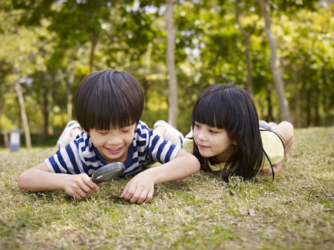 asian children playing with magnifier outdoors