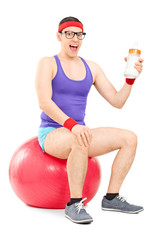 Nerdy guy sitting on fitness ball and holding milk bottle