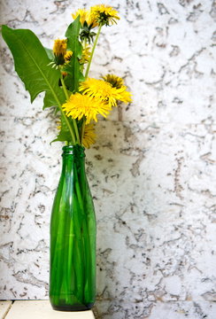 Yellow dandelions in green bottle on white cork background
