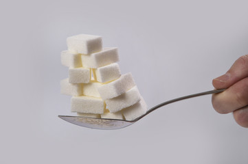hand holding spoon with stack of sugar cubes piled