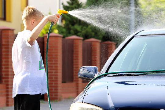 Young Boy Washing The Car With Hose