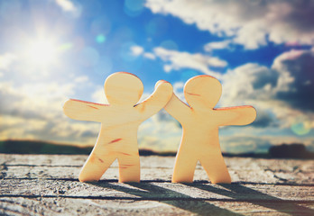 Wooden little men holding hands on sky and sun background. Symbo