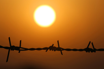 Setting sun behind barbed wire