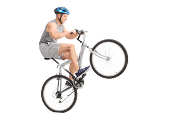 Naklejka premium Joyful young biker doing a wheelie with his bicycle