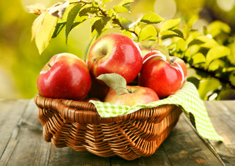 Wicker basket of red apples with napkin on nature background