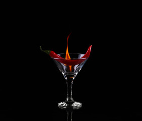 Hot chili pepper in a martini glass with a fire on a black background