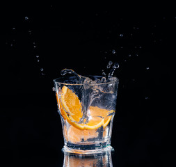 Slice of lemon splashing into a glass of water with a spray of water droplets 