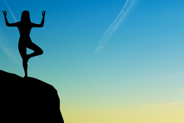 Silhouette of woman practicing yoga during sunset at the seaside.