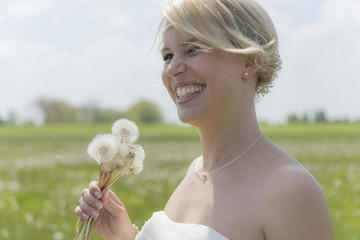Braut lacht mit vielen Pusteblumen in der Hand