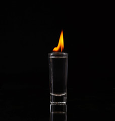 Hot chili pepper in a shot glass with a fire on a black background