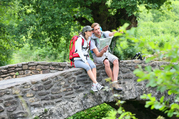 Naklejka na ściany i meble Couple of hikers reading map on stone bridge