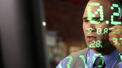 Anxious looking stock trader with ticker symbols projected across him.  Close up with dolly move past computer screen.  All ticker symbols are fictitious companies. - Powered by Adobe