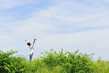 広い青空に向かって手を広げているアジア人の女性