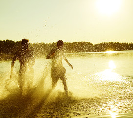 Glückliche junge Menschen laufen und springen am See beim Sonnenuntergang