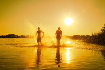 Glückliche junge Menschen laufen und springen am See beim Sonnenuntergang