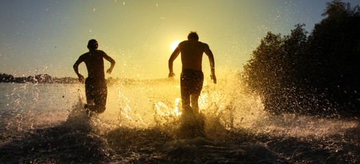 Glückliche junge Menschen laufen und springen am See beim Sonnenuntergang