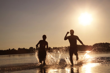 Glückliche junge Menschen laufen und springen am See beim Sonnenuntergang