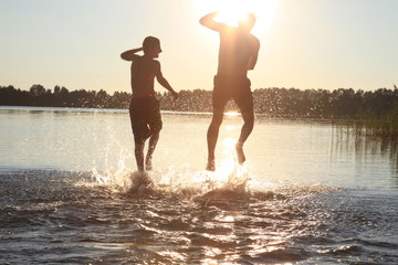 Glückliche junge Menschen laufen und springen am See beim Sonnenuntergang