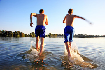 Glückliche junge Menschen laufen und springen am See beim Sonnenuntergang