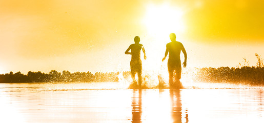 Glückliche junge Menschen laufen und springen am See beim Sonnenuntergang