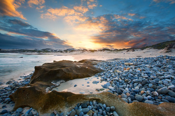 Obraz premium Early morning landscape of ocean over rocky shore and glowing su