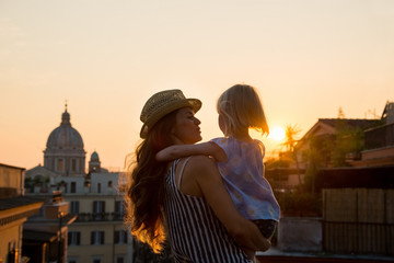 Mother in profile holding daughter in her arms overlooking Rome