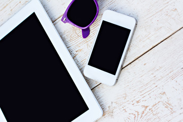 Tablet computer, mobile phone and sunglasses on a wooden table