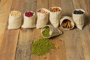 Different kinds of beans and cinnamon in sacks bag on wooden background