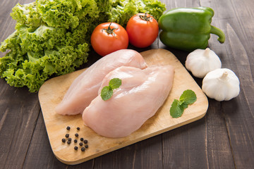 Raw chicken breast fillets and vegetable on wooden background.