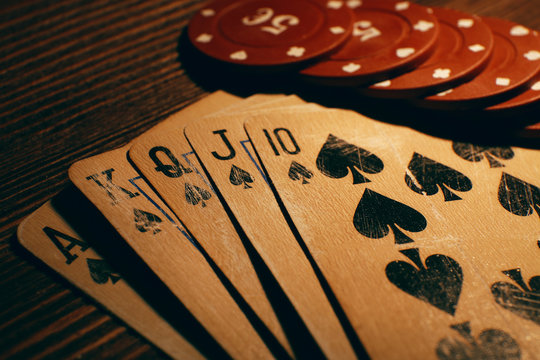 Playing cards with chips on wooden table, closeup