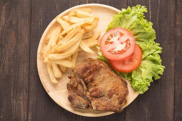 grilled pork chop steak and vegetables with french fries on wood