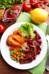 Beef with cranberry sauce, roasted potato slices, vegetables on plate, on  wooden background