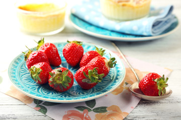 Creme brulee dessert with fresh strawberry berries on napkin, on color wooden background