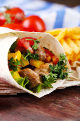 Homemade tasty burrito with vegetables and potato chips on cutting board, on wooden background