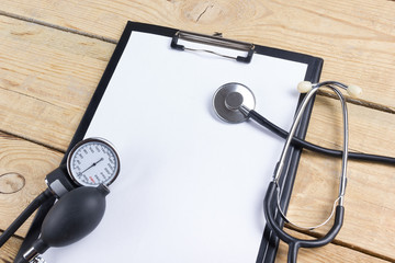 Medical clipboard and stethoscope on wooden desk background. Top view. Workplace of a doctor.