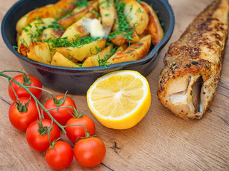 Fried fish and potatoes with dill in iron pan.